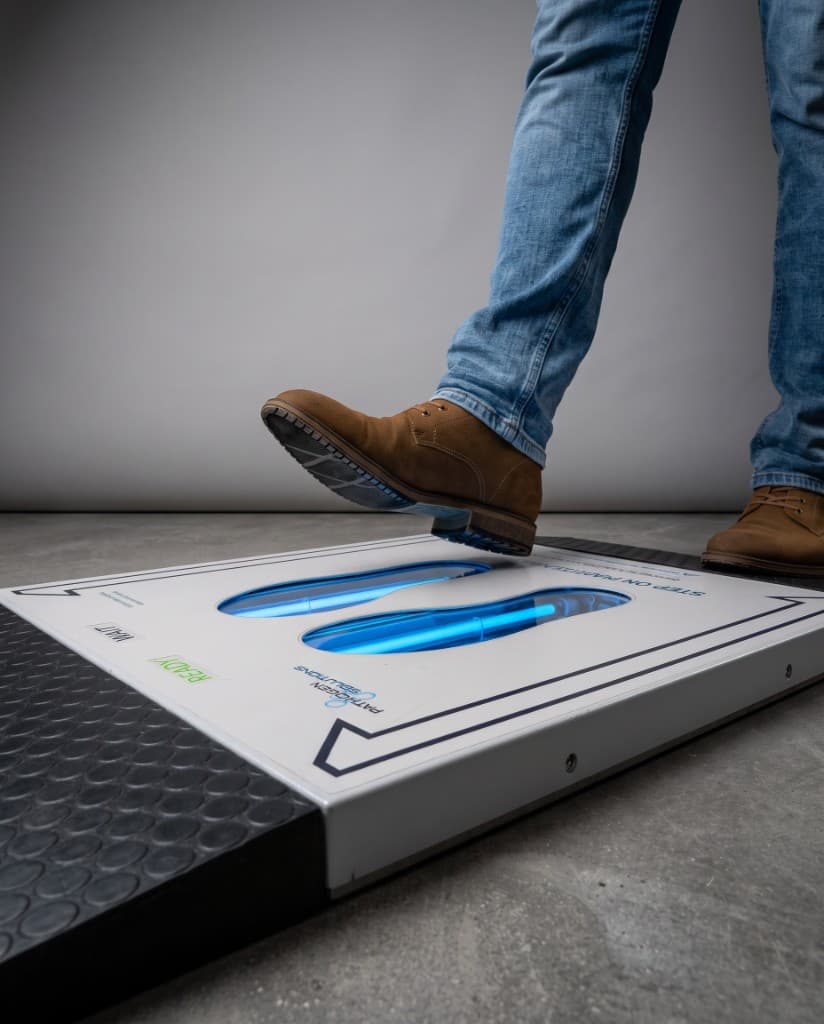 Person stepping onto PathO3Gen UVZone shoe sanitizing station with active UV-C treatment